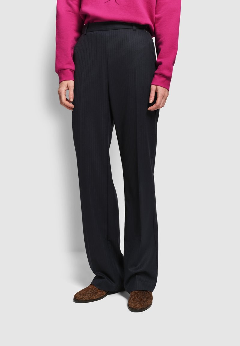 Szerokie czarne spodnie z pionowym prążkowanym wzorem i dopasowanym krojem. Noszone z jasnoróżową bluzą i butami w panterkę.