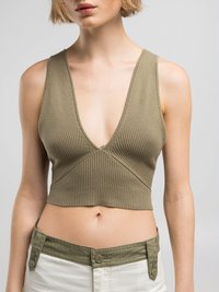 Olivgrünes geripptes Crop-Top mit tiefem V-Ausschnitt, das über ein figurbetontes Design und nähtechnische Details verfügt, kombiniert mit hellen, hoch taillierten Hosen.