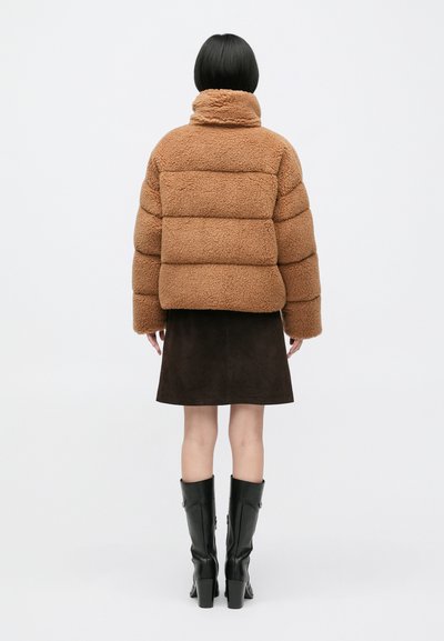Brązowa pluszowa kurtka puchowa z wysokim kołnierzem, ozdobiona poziomymi przeszyciami. Nosi się ją na ciemną zamszową spódnicę i czarne kozaki za kolano.