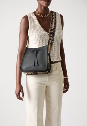 Sac seau en cuir noir avec une fermeture à cordon, doté d'une bandoulière à motif beige et noir avec du texte. Texture lisse et forme structurée.