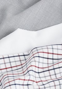 Tres tejidos superpuestos: un tejido gris texturizado, uno blanco liso y un patrón de cuadros blancos con líneas rojas y azules.