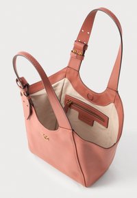 Nježna ružičasta kožna torba s dva podešavajuća remena za rame, bež tkaninska unutrašnjost i unutarnji džep na zip sa zlatnim zatvaračem.