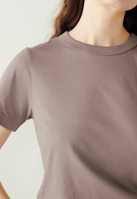 Trumpas rankovės apvalios kaklo marškinėliai švelnios mauve spalvos, pagaminti iš minkštos medvilnės audinio, pasižymintys lygiu paviršiumi ir tvarkingomis siūlėmis.
