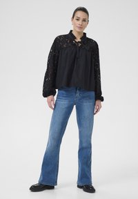 Sort bluse med lange ærmer i blonder og flæset krave, med en bundet halsudskæring. Sæt sammen med blå flagrende jeans og sorte chunky sko.