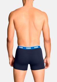 Boxer-briefs bleu marine avec une ceinture élastique blanche arborant le logo "PUMA" en bleu. Le tissu semble lisse et ajusté.