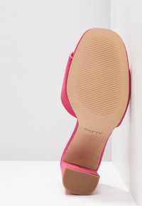 Chaussure à talons hauts en daim rose avec une semelle en caoutchouc texturée. Dotée d'un bout pointu et d'un design à l'arrière rond. Le logo de la marque est visible sur la semelle.