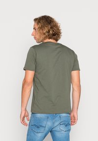 Oliven grøn bomulds t-shirt med rund hals og korte ærmer, set fra ryggen, parret med lyseblå jeans med stikninger på baglommen.