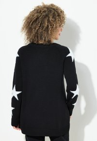 Schwarzer gestrickter Pullover mit langen Ärmeln, verziert mit großen weißen Sternmustern an den Ärmeln. Rippbündchen und Saum sorgen für Textur. Rückansicht dargestellt.