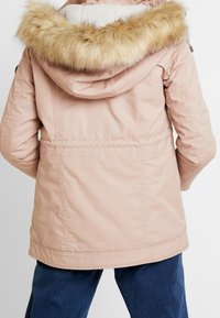 Różowa kurtka parka z kapturem obszytym sztucznym futrem, teksturowanym materiałem, elastyczną talią i detalami na szwie z tyłu. Idealna na chłodniejszą pogodę.