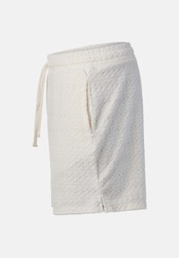 Jupe portefeuille en tissu blanc texturé avec taille à cordon et motif géométrique subtil dans un matériau doux.