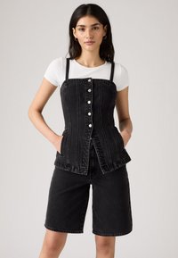Črn denim korzet z gumbi spredaj, nastavljivimi naramnicami in žepi. V kompletu s črnimi denim kratkimi hlačami, ki imajo ravno prileganje.