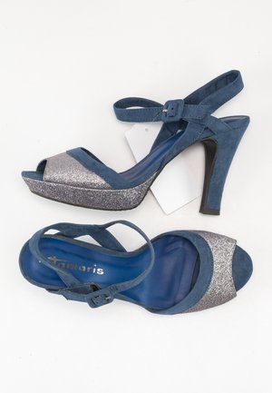 Niebieskie zamszowe sandały na wysokim obcasie z błyszczącą srebrną osłoną palców, regulowanym paskiem na kostkę i teksturowaną podeszwą dla lepszej przyczepności.