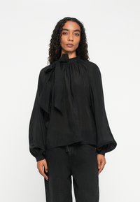 Black blouse made of lightweight fabric, featuring a high neck with a large bow, long sleeves with gathered cuffs, and a relaxed fit.