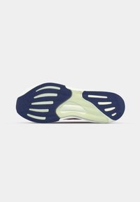 Semelle de chaussure avec des grips en caoutchouc bleu marine et vert clair et des motifs de bande de roulement, vue de dessous sur fond blanc.