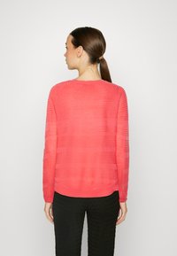 Pull en maille corail avec des rayures horizontales, col rond et manches longues, associé à un pantalon noir texturé. Détails de conception visibles au dos.