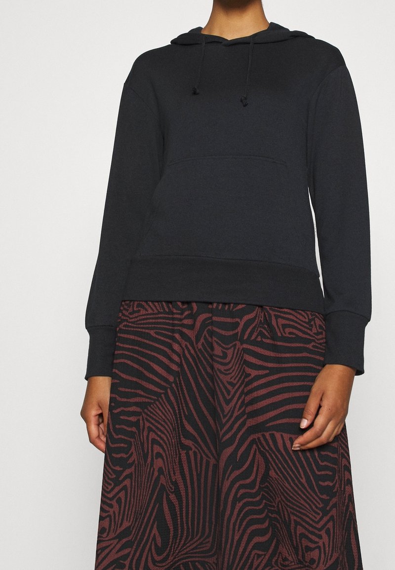 Personne portant un sweat à capuche noir avec cordons et une jupe taille haute avec un motif abstrait rayé zèbre rouge et noir.