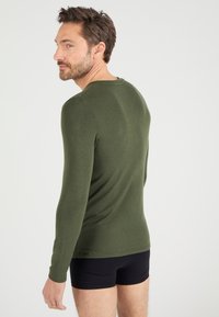 Olijfgroene blouse met lange mouwen van zacht materiaal, aansluitend ontwerp met een ronde halslijn, gecombineerd met zwarte shorts.