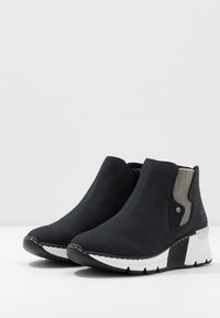 Stivali alla caviglia neri realizzati in materiale sintetico liscio, con un pannello laterale grigio testurizzato, suola a zeppa bianca e nera e cuciture decorative.