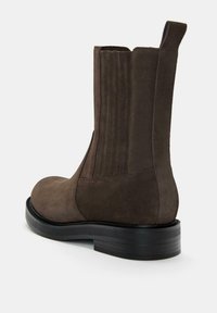 Botine din suede maro, cu vârf rotund, panouri elastice laterale și un toc din cauciuc negru texturat. Finisaj neted și detalii minime.