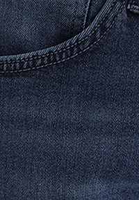 Close-up of dark blue denim fabric showing detailed stitching along the seam.