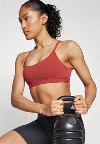 Rode sportieve crop top met dunne bandjes, gecombineerd met zwarte high-waisted shorts. De persoon houdt een zwarte kettlebell vast. Glad stofoppervlak.