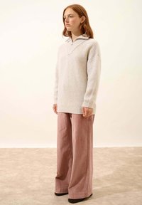 Maglione a coste grigio chiaro con colletto alto, abbinato a pantaloni in corduroy rosa a gamba larga, creando una silhouette rilassata.