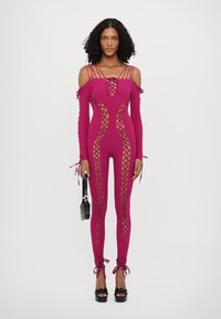 Body fuchsia cu desene tăiate, având detalii cu șireturi, mâneci lungi și bretele. Asortat cu tocuri negre platformă și geantă.