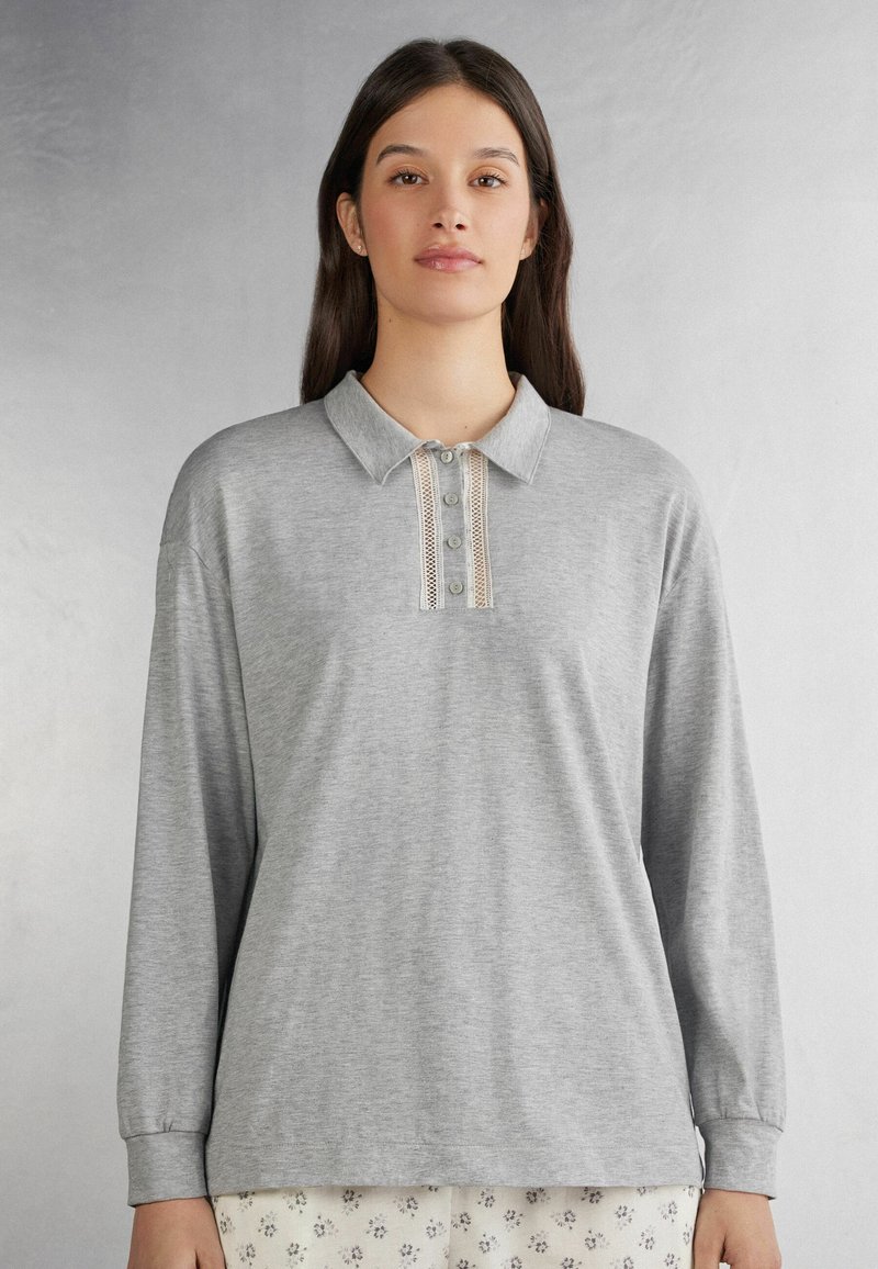 Grijs poloshirt met lange mouwen van zachte stof, voorzien van een kraag en een decoratieve knooplijst met kanten details in het midden.