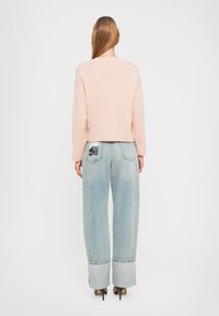 Un sweat-shirt court rose pâle avec des manches longues, associé à un jean en denim bleu clair, taille haute et à jambes larges, comportant un design de poche arrière.