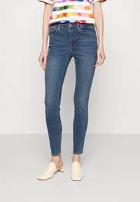 Jeans ajustados azules fabricados en denim con una textura suave, que presentan un clásico diseño de cinco bolsillos y una cintura de altura media.