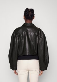 Mörkgrön lädercroppad jacka med bred krage, nedhasade axlar och synliga sömmar. Slät textur med en figurnära midjeresår.