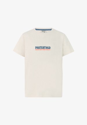Beige katoenen t-shirt met blauwe en rode tekst, gecombineerd met marineblauwe shorts. Gestructureerde stof en eenvoudig ontwerp met zijzakken. Grijze sneakers.