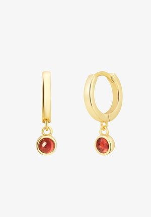 Orecchini a cerchio in oro con un grande gemma rossa sospesa da ciascun cerchio. Finitura liscia con accenti lucidi e un design di chiusura sicuro.
