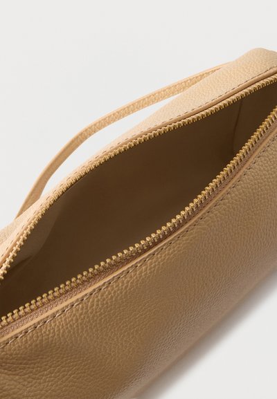 Καφέ δερμάτινο πορτοφόλι καρπού με χρυστό φερμουάρ μισάνοιχτο, που δείχνει άδειο εσωτερικό σε λευκό φόντο.