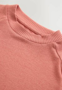 Sweatshirt rose clair avec un col rond côtelé, en tissu texturé doux, et un motif chiné subtil. Surface lisse avec un design décontracté.