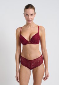 Set di reggiseno in pizzo borgogna e slip a vita alta con motivi delicati e bordi ondulati, dotato di sottili spalline regolabili e di una texture morbida.