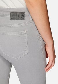 Jeans in denim grigio con una texture liscia, dotati di una tasca posteriore e di una etichetta in pelle nera del marchio vicino alla vita.