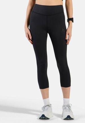 Femme portant des leggings de sport noirs courts, des chaussettes blanches et des chaussures de course blanches, avec une montre de fitness au poignet.