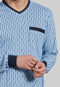 Light blue long-sleeve shirt with a V-neck, featuring a black pocket and vertical striped pattern in navy and white. Navy cuffs.