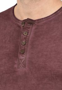 Burgunderrød bomulds henley-shirt med rund halsudskæring, fire brune knapper og en subtil tekstur med en svag glans.