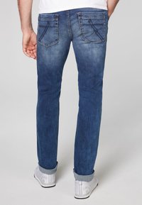 Jeans in denim blu medio con un effetto sbiadito. Presentano cinque tasche, dettagli di cucitura e orli arrotolati. Indossati con sneaker bianche.