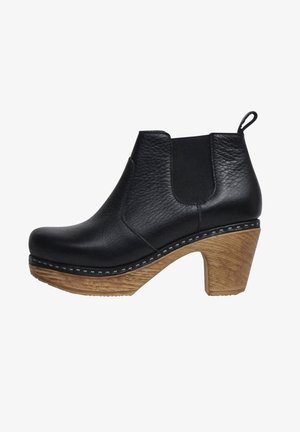 Black leather ankle boot with elastic side panels, curved wooden heel, and contrasting white stitching along the sole.