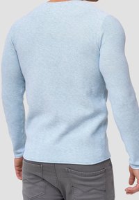 Pull-over long bleu clair texturé à manches longues avec un col rond, présentant des manches ajustées et un ourlet côtelé. Associé à un pantalon gris.