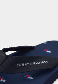 Σαγιονάρα σε ναυτικό μπλε με μαύρο υφασμάτινο λουρί, που φέρει μικρά λογότυπα Tommy Hilfiger στην σόλα και το όνομα του brand στο λουρί.