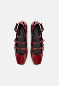 Ballerines Mary Jane en cuir verni rouge brillant avec doubles sangles à boucles et bouts carrés, vues de dessus sur un fond blanc.