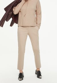 Pull côtelé beige, pantalon tailleur beige, et chaussures habillées noires avec embout métallique. Veste en cuir posée sur le bras.