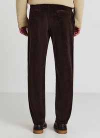 Pantalons en velours côtelé marron avec une texture douce, dotés de deux poches arrière et d'une coupe décontractée. Associés à des chaussures foncées et un pull beige.