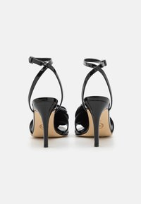 Sandaalit mustasta patenttinahasta, joissa on avonainen takaosa, ohuet nilkkahihnat ja kaareva etusuunnittelu. Varustettu 10 cm:n stilettokorkeudella.