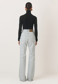 Šviesiai pilki džinsai su aukštu liemeniu ir tiesia forma, derinami su juoda ilgomis rankovėmis turtlenoku. Yra nugarinė detalė ir dvi gale esančios kišenės.