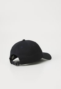 Mørkeblå bomullskaps med buet skjerm, justerbar stropp bak og en stoffbelagt knapp på toppen. Minimalistisk design.